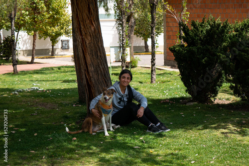 Peruvian Woman Sitting on the Grass, Hugging a Brown and White Mongrel Dog and Surrounded by Lots of Nature
