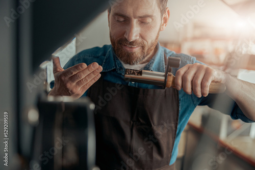 Close up of business owner inhaling aroma of coffee in own manufacturing of roasted coffee beans