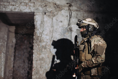 Portrait of a Ukrainian defender in the dugout. A soldier with a weapon in his hands casts a shadow on the wall.