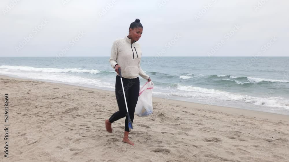 Mixed race woman picking up litter, including a discarded face mask, from the bech. Mixed race woman picking up litter, including a discarded face mask, from the bech.