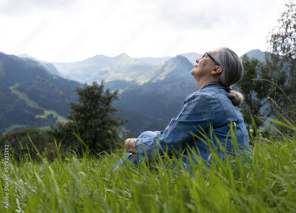 An elderly woman in a denim suit sits on a alpine meadow and looks at the sky An elderly woman in a denim suit sits on a alpine meadow and looks at the sky