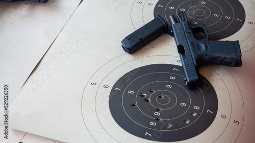 A black handgun and a paper target with bullet marks.