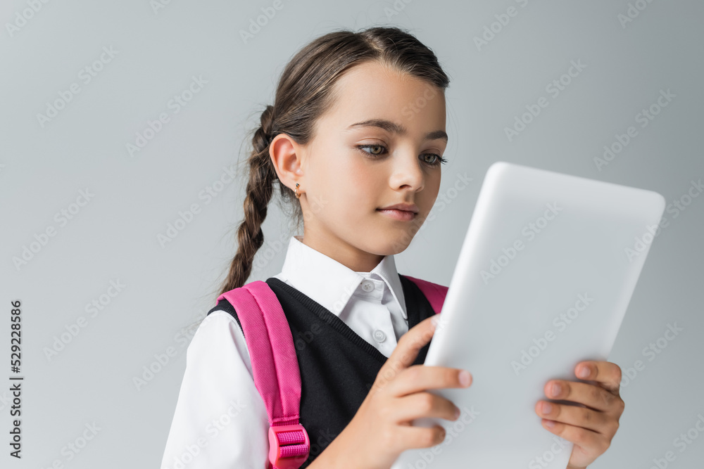 cute girl in school uniform with backpack using digital tablet isolated on grey. cute girl in school uniform with backpack using digital tablet isolated on grey.