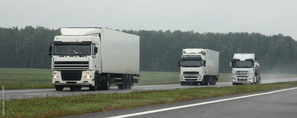 Semi trucks lorry convoy overtake on wet asphalted highway front view. Traffic safwty on rain slippery road