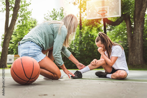 Mother and little daughter play basketball outside crying because of ankle accident photo
