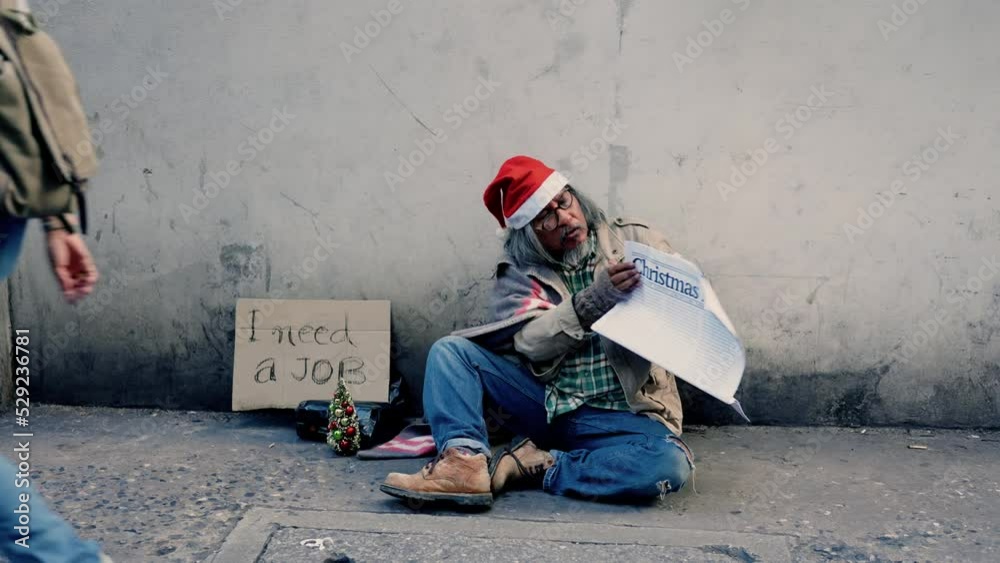 4k, A homeless man, an old Asian man wearing a red Christmas hat, is sitting on the ground reading a newspaper, next to the wall lined with job boards and many passers. Look for jobs from newspapers.