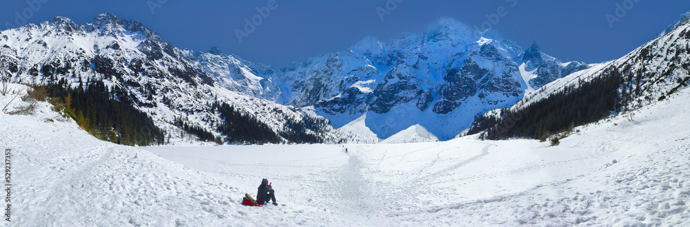 Obraz premium panoramic view of morskie Oko lake covered in ice. girl drinking tea against the backdrop of Tatra Mountains. Zakopane, Poland