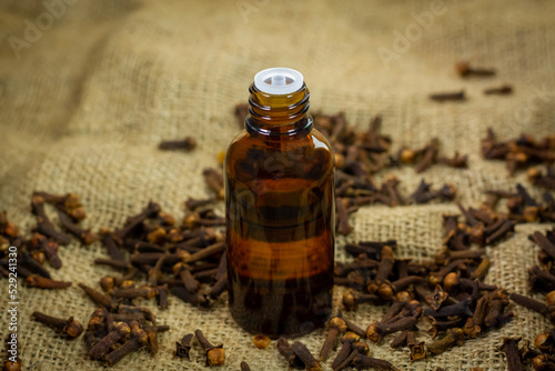 Essential oil of cloves in bottle and dry cloves on burlap background.