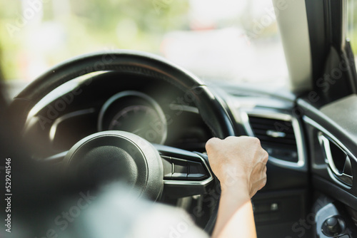 Close up of woman driving hand holding steering wheel in blur background.