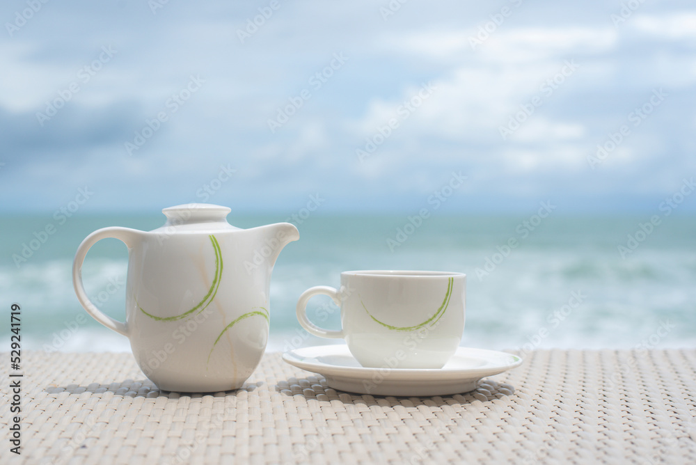 cup and pot of tea on wood table sea background.