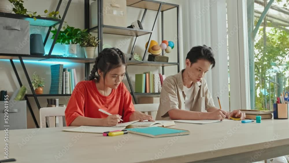 Asian girl and boy sitting at desk in classroom and writing in workbooks while studying at school Asian girl and boy sitting at desk in classroom and writing in workbooks while studying at school