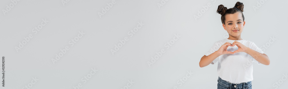 cheerful girl with glitter stars on cheeks showing heart with hands isolated on grey, banner. cheerful girl with glitter stars on cheeks showing heart with hands isolated on grey, banner.