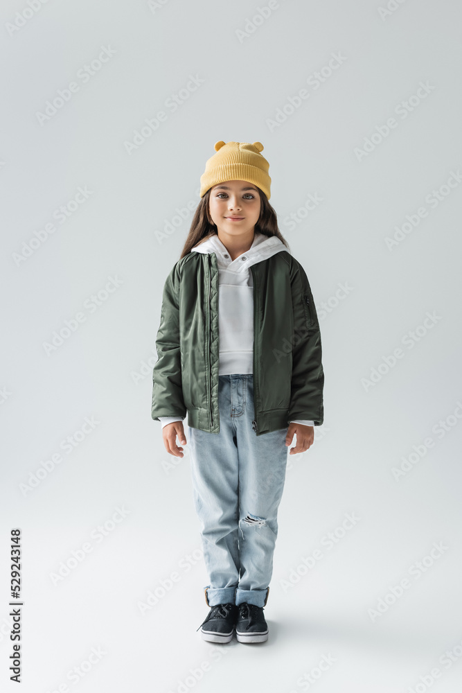 full length of adorable girl in trendy autumnal outfit smiling and standing on grey. full length of adorable girl in trendy autumnal outfit smiling and standing on grey.