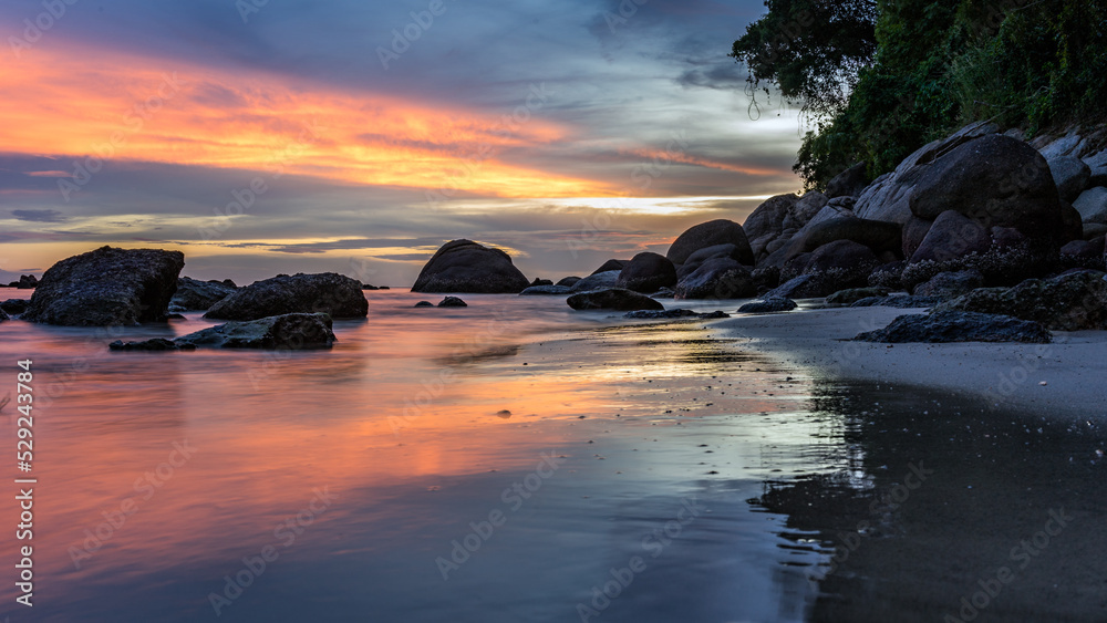 Obraz premium Scenic saturated seascape with stones in sea water on shore at beautiful colorful sunset on beach. Long exposure. Phuket, Thailand