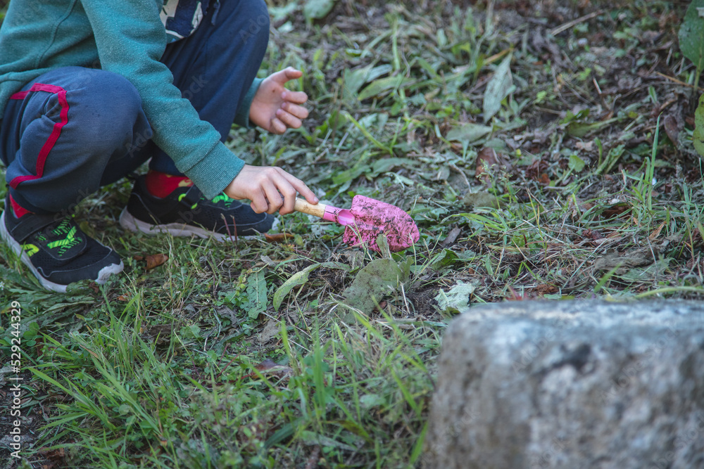 Naklejka premium Child playing in the dirt with gardening supplies. Concept of happy childhood, contact with nature, discovery and learning.