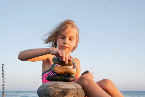 A girl sits on the seashore at sunset and plays with stones. photo