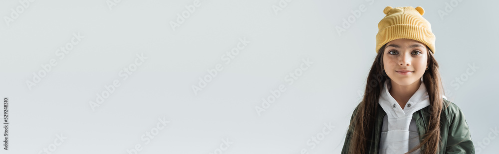 portrait of cheerful kid in beanie hat and bomber jacket looking at camera isolated on grey, banner. portrait of cheerful kid in beanie hat and bomber jacket looking at camera isolated on grey, banner.