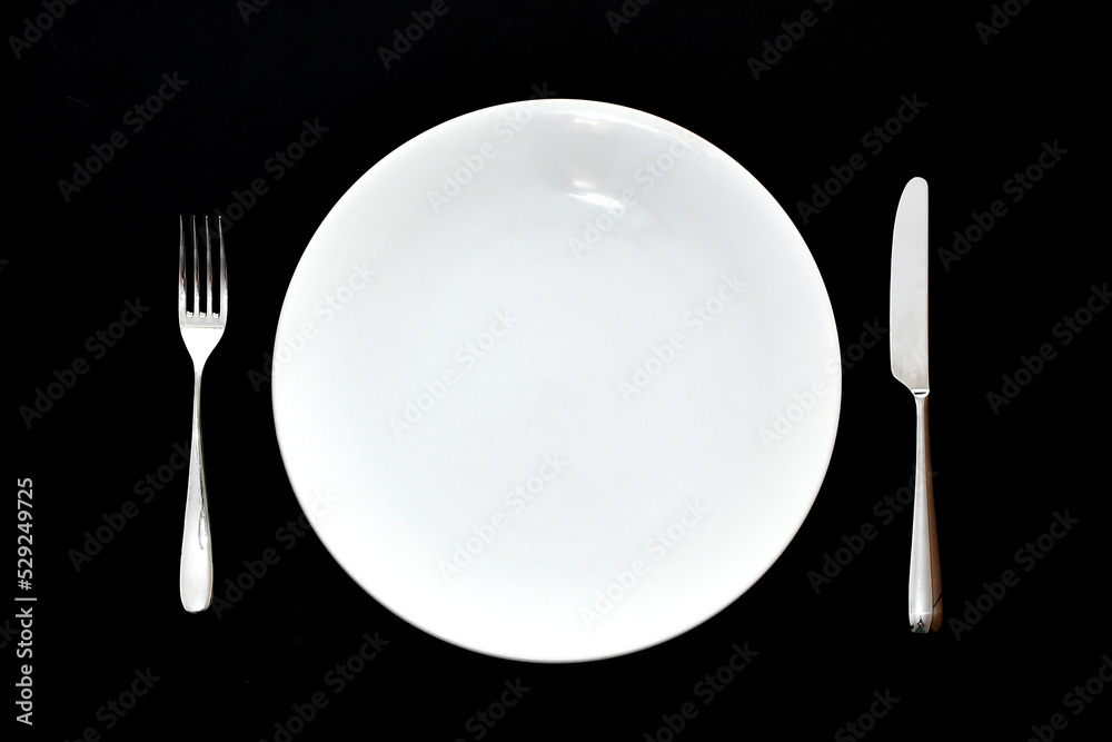 Stainless steel knife and fork and empty white dinner plate on a plain back background. No people.