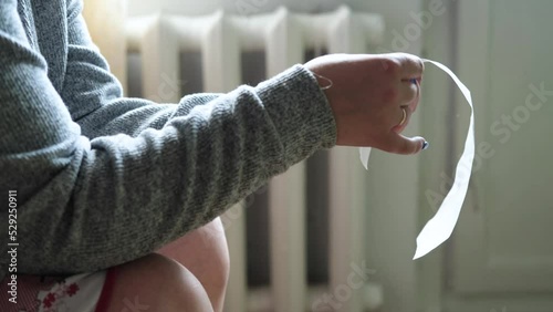 A woman in a warm sweater sits at home in front of the battery and holds a gas bill in her hands. Energy crisis concept. Slow motion video