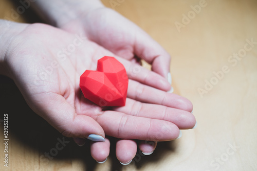 Adult holding red heart in hands over a wooden table. Family relationships,health care,cardiology concept,heart health care concept