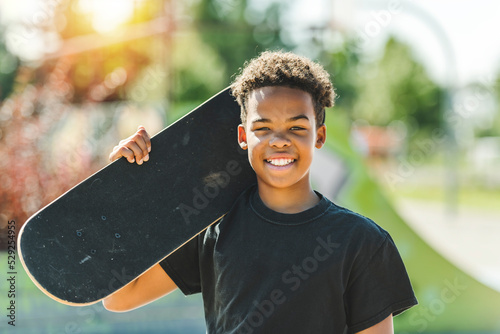Afro-American boy with black t-shirt posing with his skateboard with the sky in the background