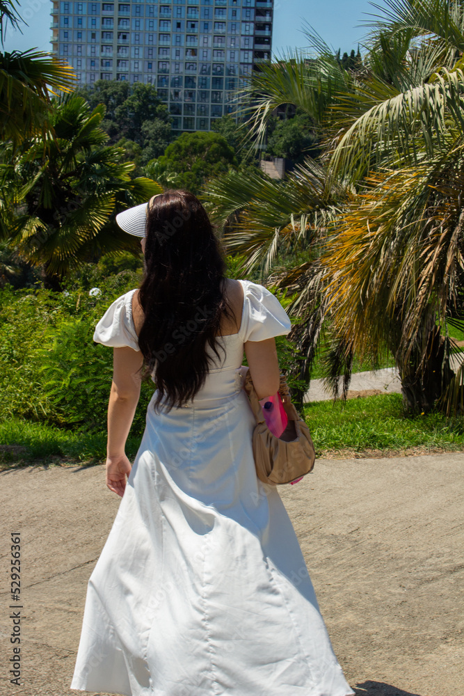 Beautiful black-haired girl in a white dress on a walk in her garden