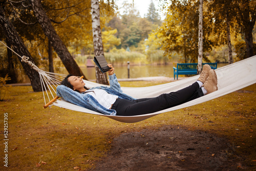 Cheerful portrait of beautiful asian woman enjoy relax lay down on hammock on nature forest woods outdoors park and smiling to tablet - roaming connection and smart working job