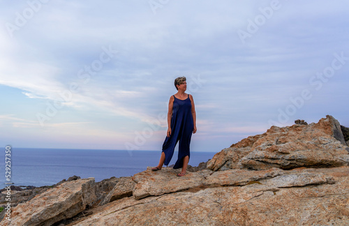 Mujer en unas rocas con una vista del mar al aire libre en la playa con un perro en los brazos