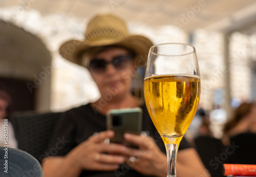 Mujer con un sombrero de paja sentada en una terraza de un bar tomándose una cerveza mientras mira su teléfono móvil