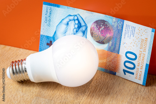 Swiss money 100 francs and a light bulb, concept of rising energy and electricity prices in Switzerland