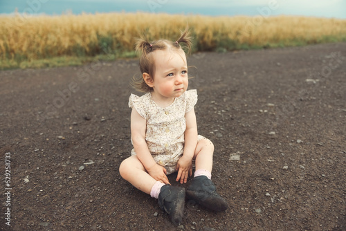 Happy little girl sits on the road outdoors.
