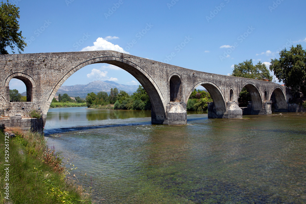 The Bridge of Arta. A stone bridge that crosses the Arachthos river  in the west of the city of Arta in Greece. Sunny day with blue sky