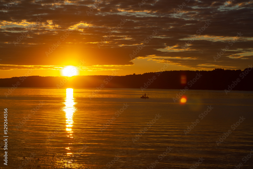 Bright sunset in the river, orange sky in dark clouds and reflection of the sun in the water