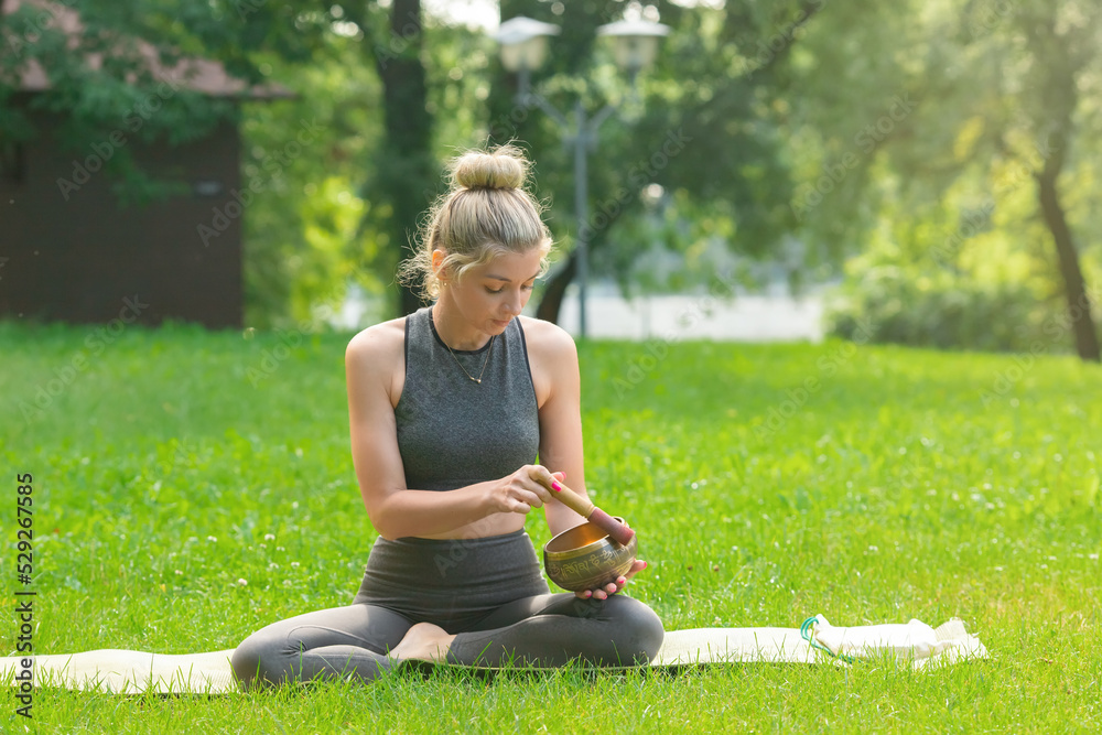 A beautiful woman sitting on the green grass , holds a meditation bowl, drives a stick on it. A beautiful woman sitting on the green grass , holds a meditation bowl, drives a stick on it.