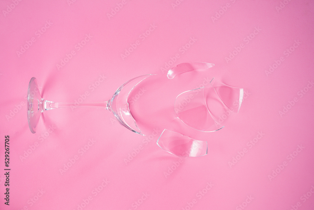 Broken champagne glass with splinters on pink background. Wineglass fallen and shattered into smithereens with sharp glass edges. Concept fight against alcoholism. Creative top view.