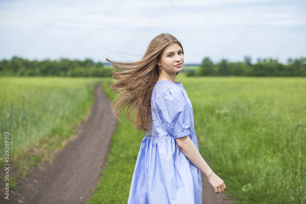 Portrait of a young blonde woman in blue dress walking in summer parkpark