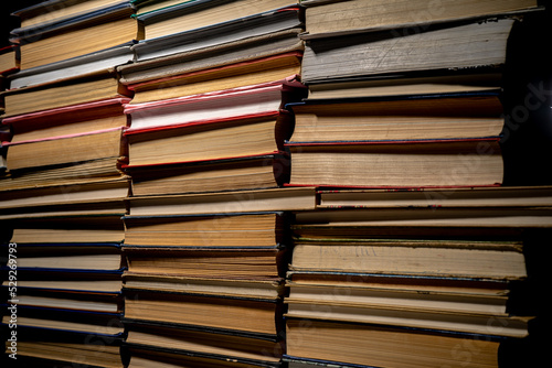 Shelves with old books. Stacks of textbooks with red, blue, green covers and paper sheets with shadow in a dark library. Stacked retro books in a bookstore.