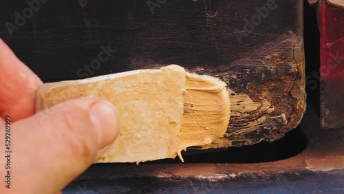 A man's hand with a spatula applies putty on a rusty fender of a car. Medium plan photo