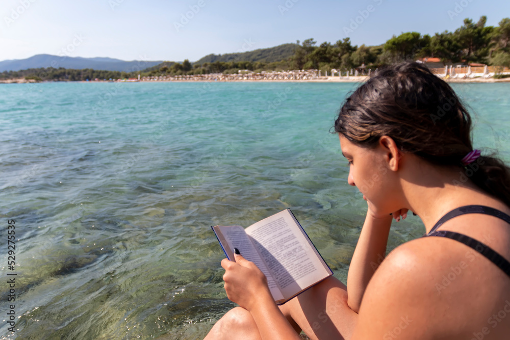 Teen girl reading a book and relaxing at the beach