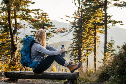 Woman resting on bench in forest. Relaxation during hiking in mountain photo