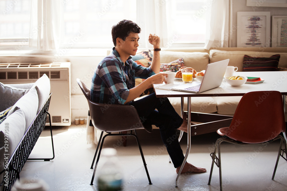 Side view of man using laptop while having breakfast at home Side view of man using laptop while having breakfast at home