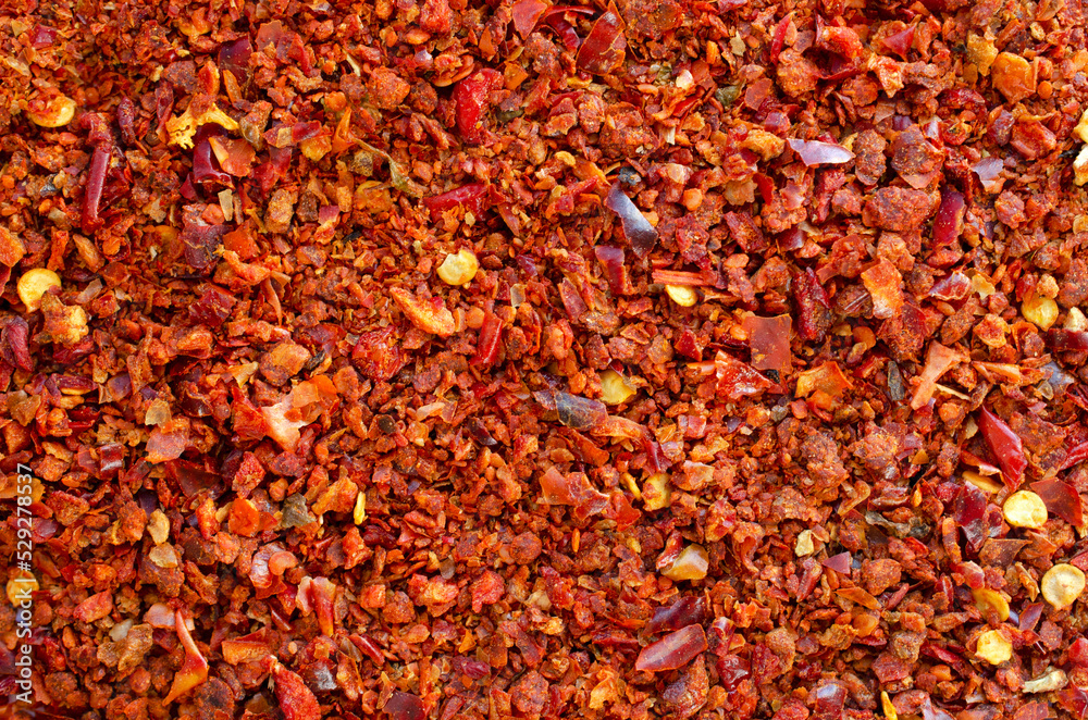 Background of crushed red cayenne pepper, dried chili flakes and seeds, top view. Ground red chili pepper, texture, background. Pile of crushed red peppers, background, top view.