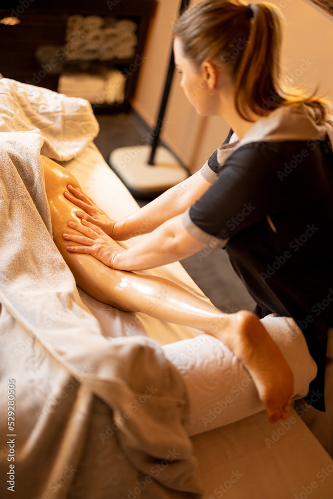 Woman receiving professional recovering and anti-cellulite massage on her legs at Spa salon. Client lying covered with towel on medical couch, close-up on leg