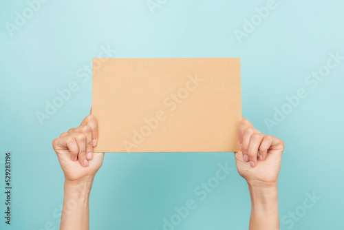 Woman hands holding blank rectangular sheet of brown cardboard on light blue background