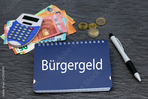Das deutsche Wort Bürgergeld steht auf einem Notizblock mit Taschenrechner und Euro Banknoten. Neues finanzielles Hilfesystem für Arbeitslosigkeit in Deutschland