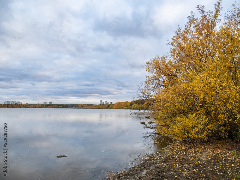 Autumn lake with trees on the shores. Reflection of blue sky with clouds in water.