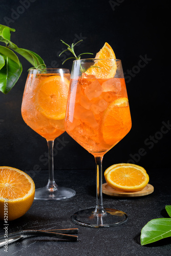 Fototapeta Naklejka Na Ścianę i Meble -  Classic italian aperitif aperol spritz cocktail in two wineglasses with ice cubes and slice of orange on black stone background, traditional summer fresh iced drink, closeup
