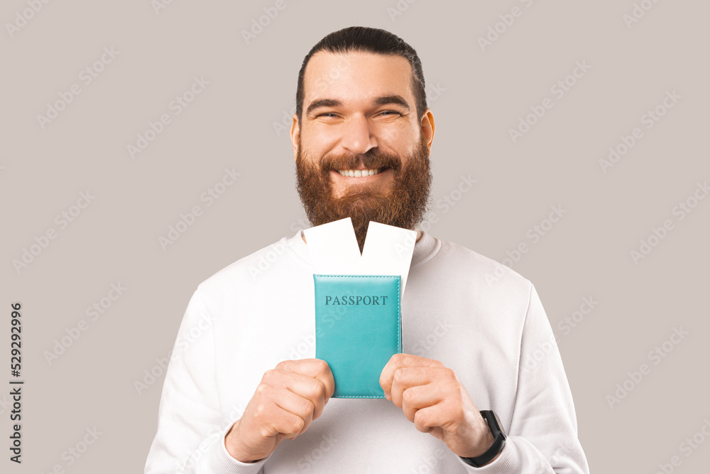 Φωτογραφία Pleased bearded man is holding passport with two tickets in front of him