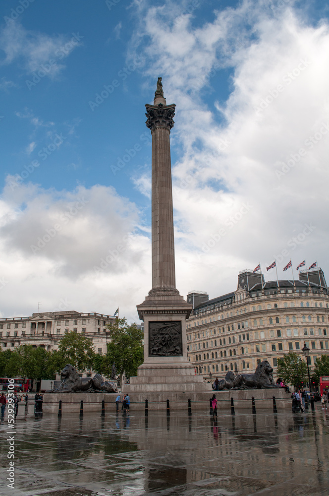 Trafalgar Square in London with puddles and blue sky. A tall concrete column as a tourist monument.