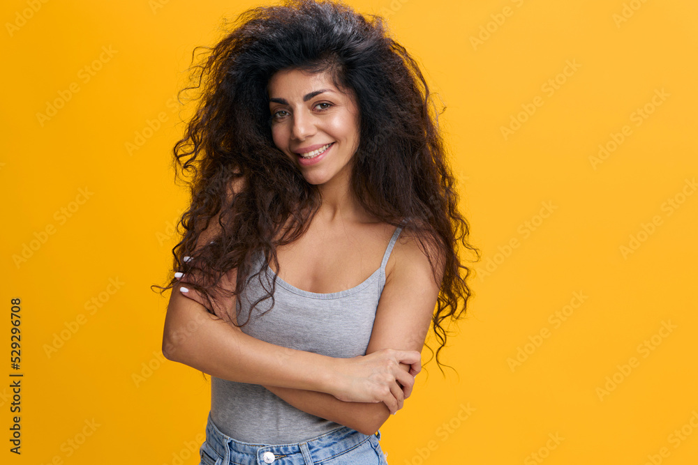 Portrait Of Confident Young Woman With Curly Hair Posing With Folded Arms Over Yellow Background In Studio, Beautiful Millennial Lady With Tanned Skin Looking And Smiling At Camera, Copy Space Portrait Of Confident Young Woman With Curly Hair Posing With Folded Arms Over Yellow Background In Studio, Beautiful Millennial Lady With Tanned Skin Looking And Smiling At Camera, Copy Space